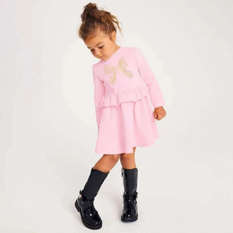 Toddler girl wearing pink cotton dress with bowknot and ruffles, styled with black boots