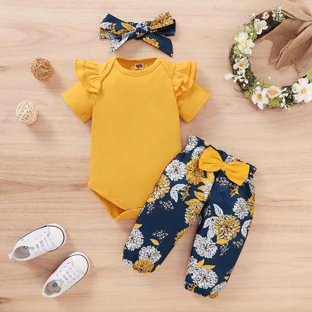 Newborn baby girls' clothing set with yellow short sleeve bodysuit, floral navy pants with yellow bow, and matching headband.